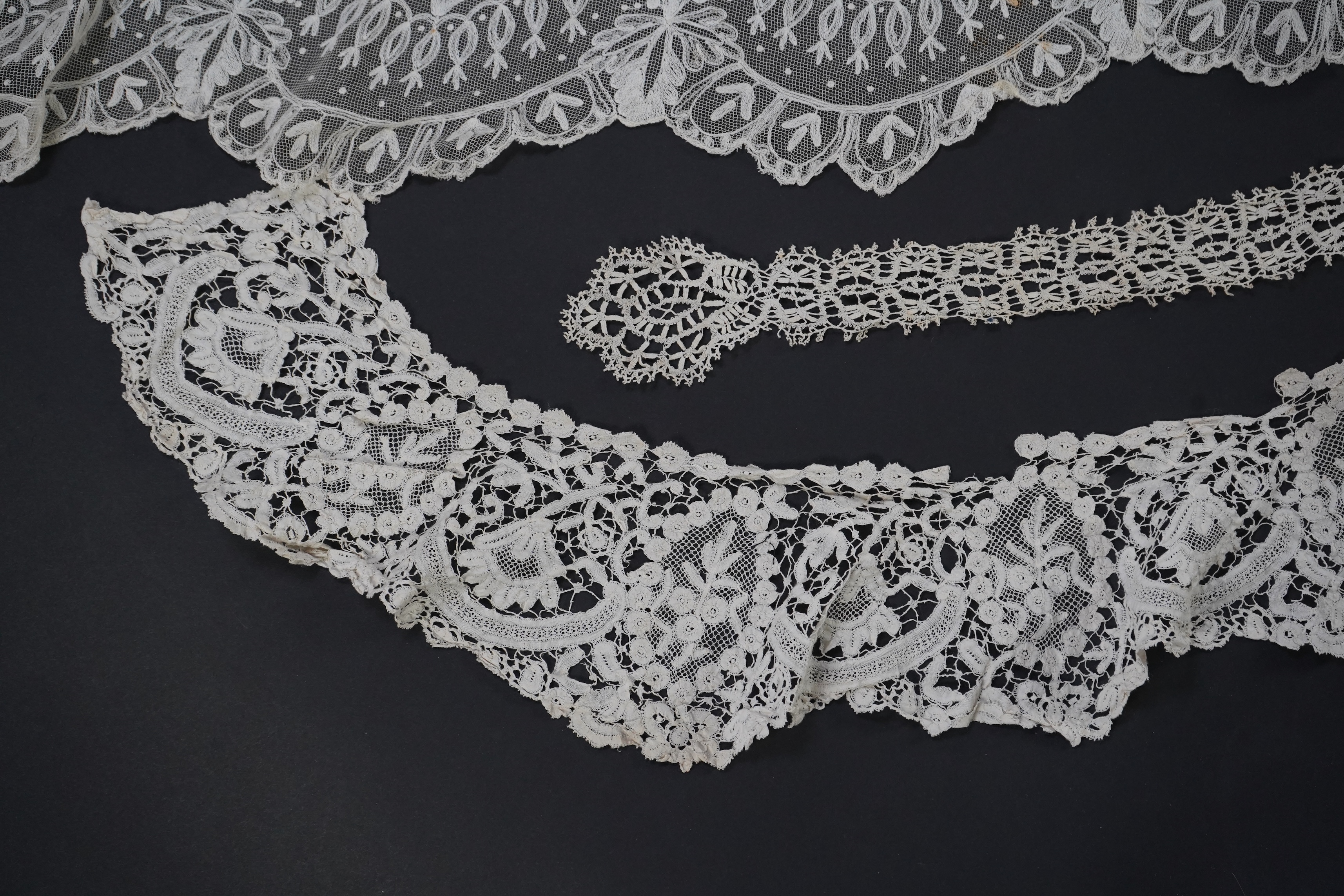 A white tape lace on net bed cover, a cream lace needle run panel, three Brussels bobbin lace collars, a lappet and two beaded tea pot covers, bed cover 200cm x 250cm. Condition - the bedcover has damage to the netting,